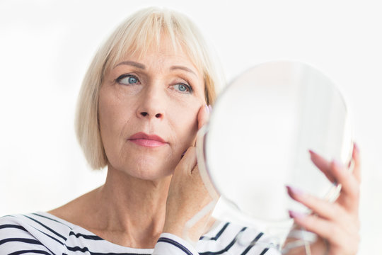 Elderly woman applying face cream, looking at mirror