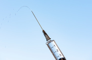 Medical Syringe needle and small drops. Isolated on blue background. Macro