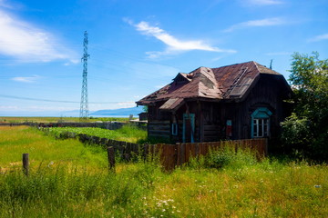 Summer landscape with old wooden abandoned house and garden in russian village on coastline Baikal lake. Cute rural landscape in the hot summer afternoon. Pastoral picture