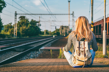 Backpacker woman sitting on railway station platform and waiting for train - obrazy, fototapety, plakaty