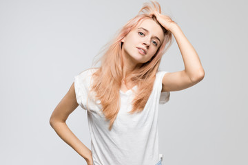 Fototapeta premium Studio portrait of cute young blonde woman in white t-shirt frowning her face in displeasure, straightens hair with hand/closed posture, angry, strict and skeptical expression, negative emotion.