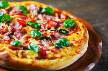 Pizza with Mozzarella cheese, ham, pepper, olive, meat, Tomato sauce, Spices and Fresh Basil. Italian pizza on wooden background