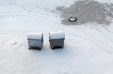 Metal old garbage cans are standing in the yard in the snow in winter
