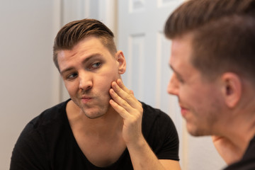 Good Looking Young Man Looking and Examining His Beard and Face in His Home Bathroom Mirror in the Morning Getting Ready for a Good Day