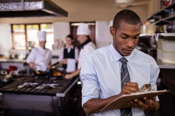 Male manager writing on a clipbaord in kitchen