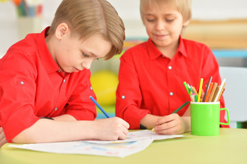 Two smiling boys in red shirts drawing with pencils 