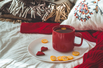 Obraz na płótnie Canvas Red cup of tea with kumquat and two hearts cookies on a white bed. Cozy Home. Valentines day concept