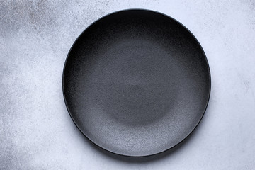 Empty black plate on gray concrete background. Top view, with copy space - obrazy, fototapety, plakaty