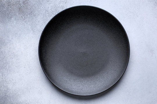 Empty black plate on gray concrete background. Top view, with copy space