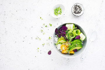 Vegetables rice bowl salad. Avocados, cucumbers, cherry tomatoes, rice, herbs, sesame for spring snack. Top view. On a light background.