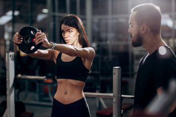 Athletic girl  doing exercise for the muscles of the arms with weight in the gym under the supervision of a coach
