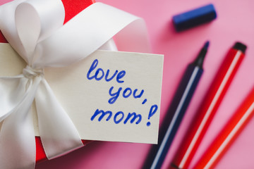 Red gift box tied with a white ribbon, markers and a card with an inscription  