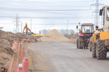 Road transport works, repair, laying a thick layer of asphalt, concrete, large trucks, tractors, road markings, red and yellow road signs, heaps of sand, earth, old buildings, people make the way © Kurganskiy