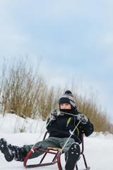 Fototapeta na wymiar Happy small boy in winter snow covered courtyard