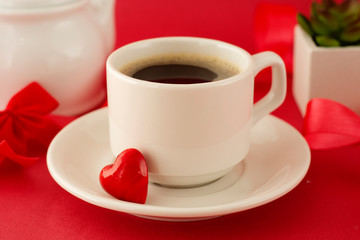 Valentine's Day breakfast. Cup of coffee over deep red background with red letter, decorative heart and plant. Top view.