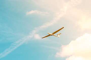 Glider flying against the blue sky with clouds and sunlight