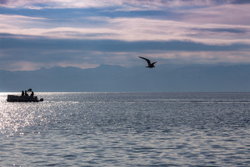 Fototapeta na wymiar Landscape in silver-pink-blue on the beautiful Ohrid Lake with silhouettes of а boat and flying seagull. Macedonia.