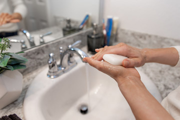 Young Caucasian Female Hands Lathering White Bar Hand Soap for Washing and Personal Hygiene, and Then Rinsing Hand Under Sink Water at Clean Home Bathroom