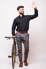 Fototapeta na wymiar Portrait of a bearded handsome young man walking with fixie bicycle and wave hello gesture over white background