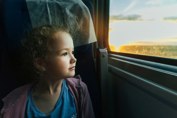 Beautiful little girl looking out train window outside, while it moving. Going on vacations and...
