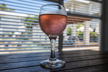 Rose wine glass on a table with blinds in the background
