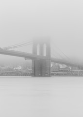 Black an white photo of Brooklyn bridge from east river on a foggy day with long exposure