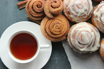 Fresh pastry. Cinnamon rolls and a Cup of tea on a wooden table. Fresh homemade nuns with cinnamon, a cup of tea, cinnamon sticks. Selective focus, close-up