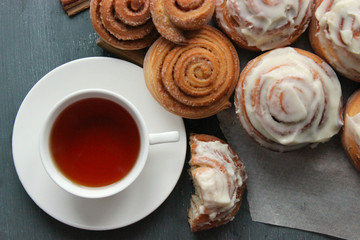 Fresh pastry. Cinnamon rolls and a Cup of tea on a wooden table. Fresh homemade nuns with cinnamon, a cup of tea, cinnamon sticks. Selective focus, close-up