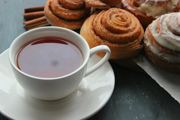 Fresh pastry. Cinnamon rolls and a Cup of tea on a wooden table. Fresh homemade nuns with cinnamon, a cup of tea, cinnamon sticks. Selective focus, close-up