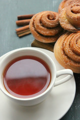 Fresh pastry. Cinnamon rolls and a Cup of tea on a wooden table. Fresh homemade nuns with cinnamon, a cup of tea, cinnamon sticks. Selective focus, close-up