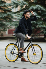 Fototapeta premium Full length photo of smiling young bearded man riding a bicycle on the city street