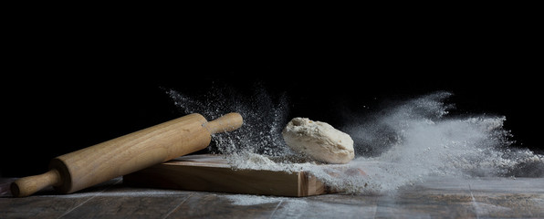 Studio photo of a ball of bread dough falling on flour with roller