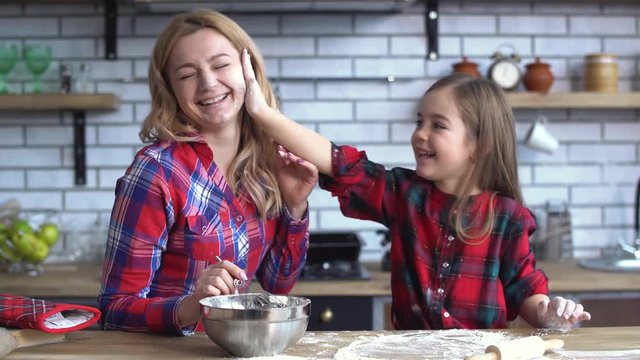 Happy mother with daughter play in kitchen, small girl put flour on mamas face