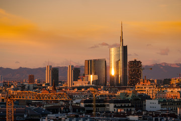 Obraz premium Milan skyline at sunset with modern skyscrapers in Porta Nuova business district in Italy. Panoramic view of Milano city. The mountain range of the Lombardy Alps in the background.