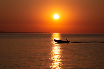 Fototapeta premium Sunnrise sun with fishermans boat in sunlight way on sea surface.