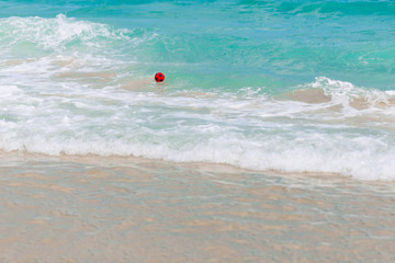 Obraz premium A red rubber soccer ball is floating in the ocean. The waves carry the ball to the shore.