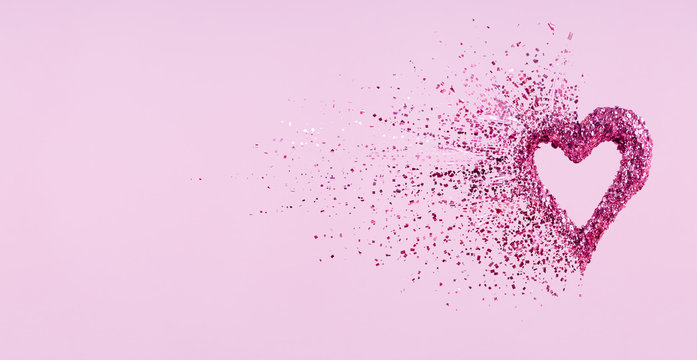 Glitter heart dissolving into pieces on pink background.  Valentines day, broken heart and love emergence concept
