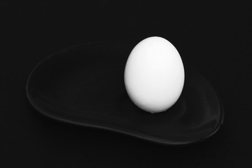 Black and white. White egg on black exclusive clay plate on black background. Minimalism style. Black and white photo.