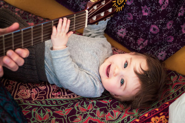 baby is making music with a guitar at home