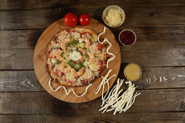seafood pizza with shrimps and mozzarella cheese on a wooden plate on a wooden rustic table. Mediterranean food. Vegetarian. Flat lay. Top view. With copy space for text.