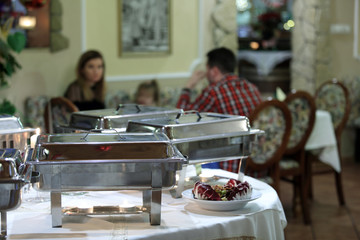 Patelnie z jedzeniem w restauracji na szwedzkim stole, ludzie w czasie kolacj.
