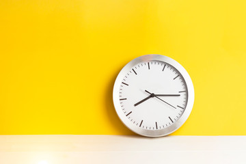 Metal alarm clock on a yellow background and wooden white table. Free place for text or logo, copyspace. Toned sunlight