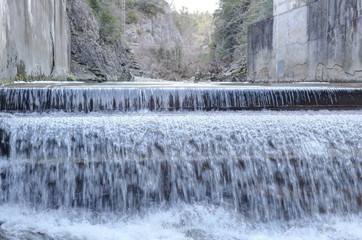 A small waterfall over concrete in the Veral river with grey rock and cold ice stalactites in the Foz de Binies zone, during winter, in Aragon, Spain