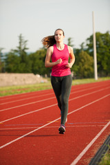 Obraz premium Beautiful young woman runner run on a track in early summer afternoon
