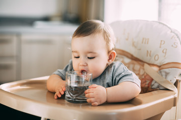 A child on a high chair drinking water from a glass - Powered by Adobe