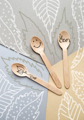 Eco-friendly organic disposable utensils made of bamboo wood. Disposable spoons with an inscription and drawings. Concept leaves background.