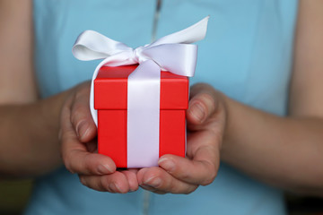 Woman with gift box in her hands. Girl in blue dress holding present in red packaging tied with white ribbon, concept of birthday, surprise or Valentines day