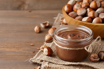 Chocolate spread with hazelnuts on wooden background