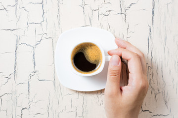 Female hand holding coffee cup on white kitchen table. Coffee cup espresso for breakfast. Top view,...