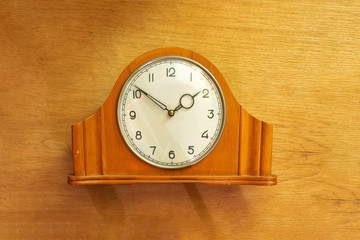 Old table clock made of wood. Mechanical. On a wooden background.